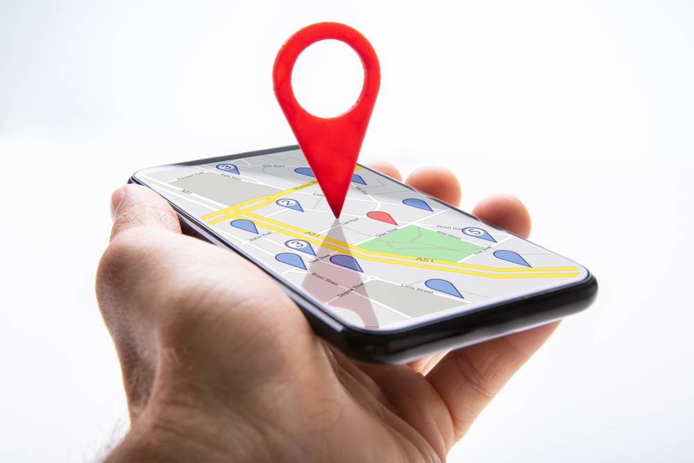 Close-up Of A Person's Hand Holding Cellphone With Red Map Pin Pointer Against White Background